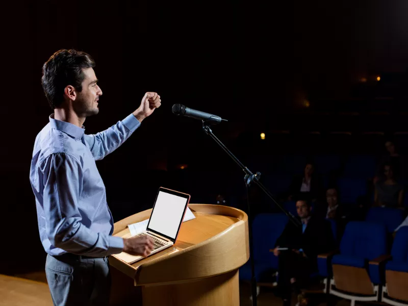 Speaker delivering a powerful talk on motivational speech topics to a live audience in an auditorium.<br />
